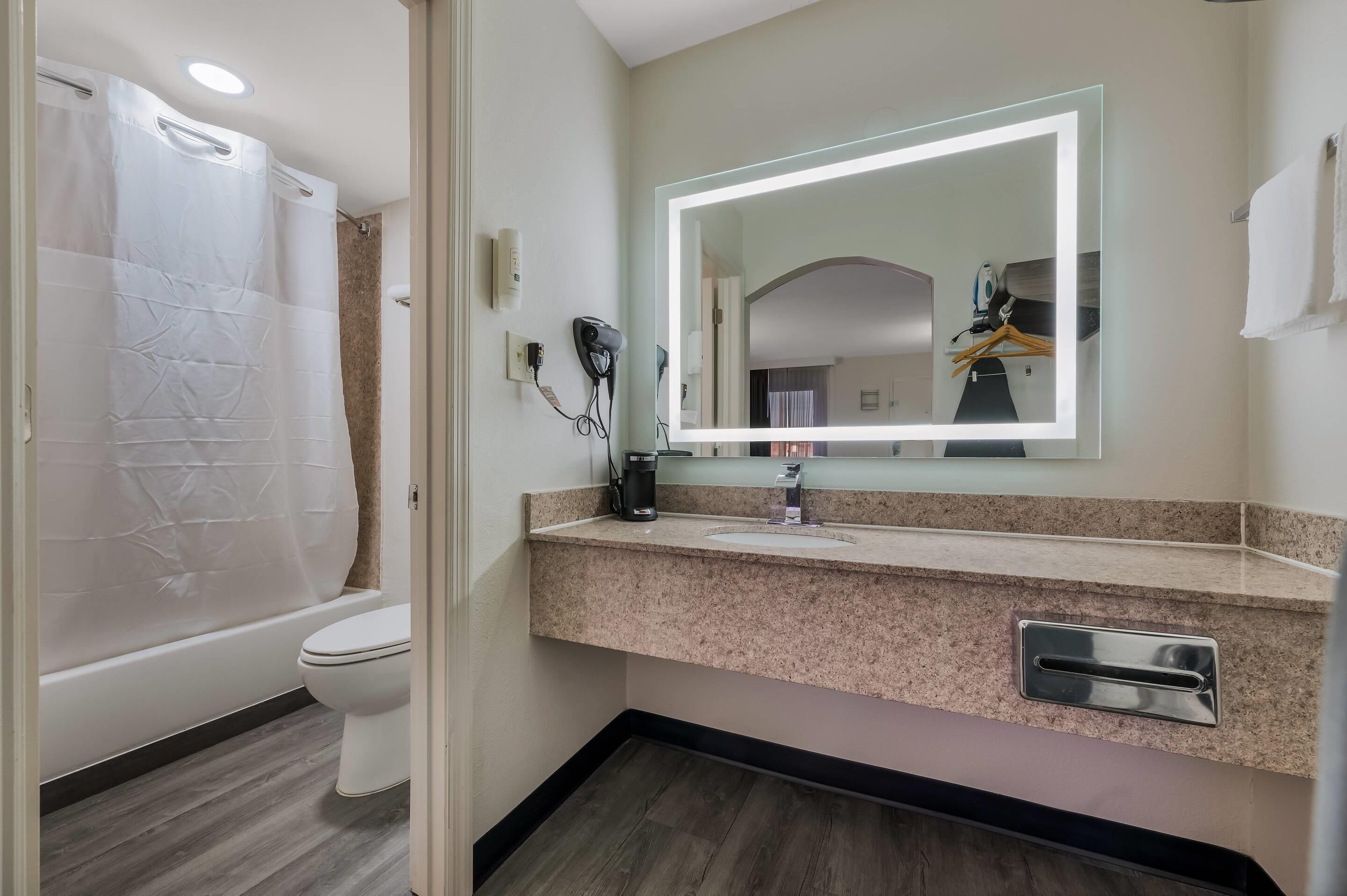 A bathroom with a shower, toilet, vanity with a mirror, and a towel rack.
