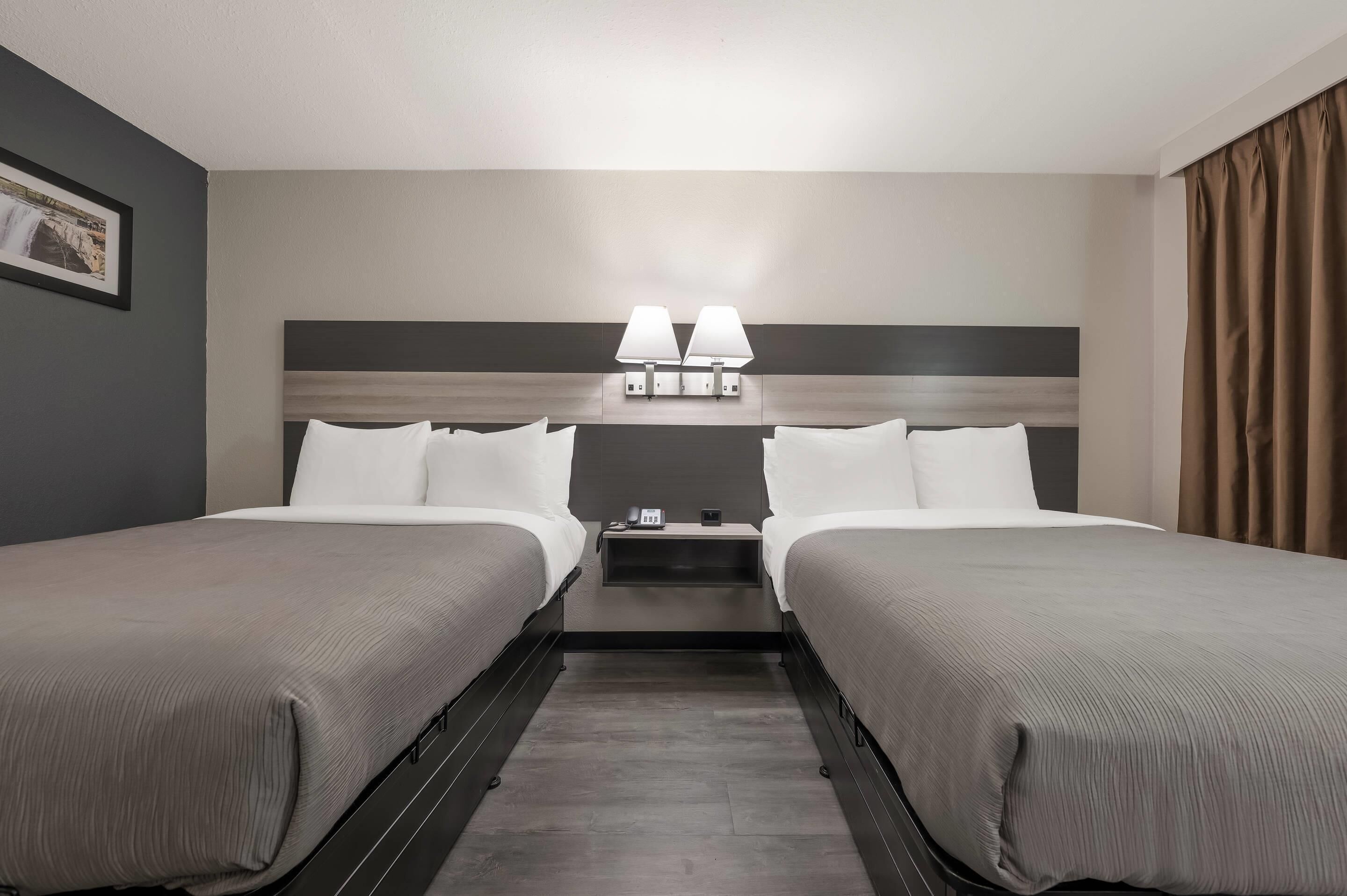 A hotel room with two beds, a nightstand, two bedside lamps, a framed picture on the wall, and a window with curtains.
