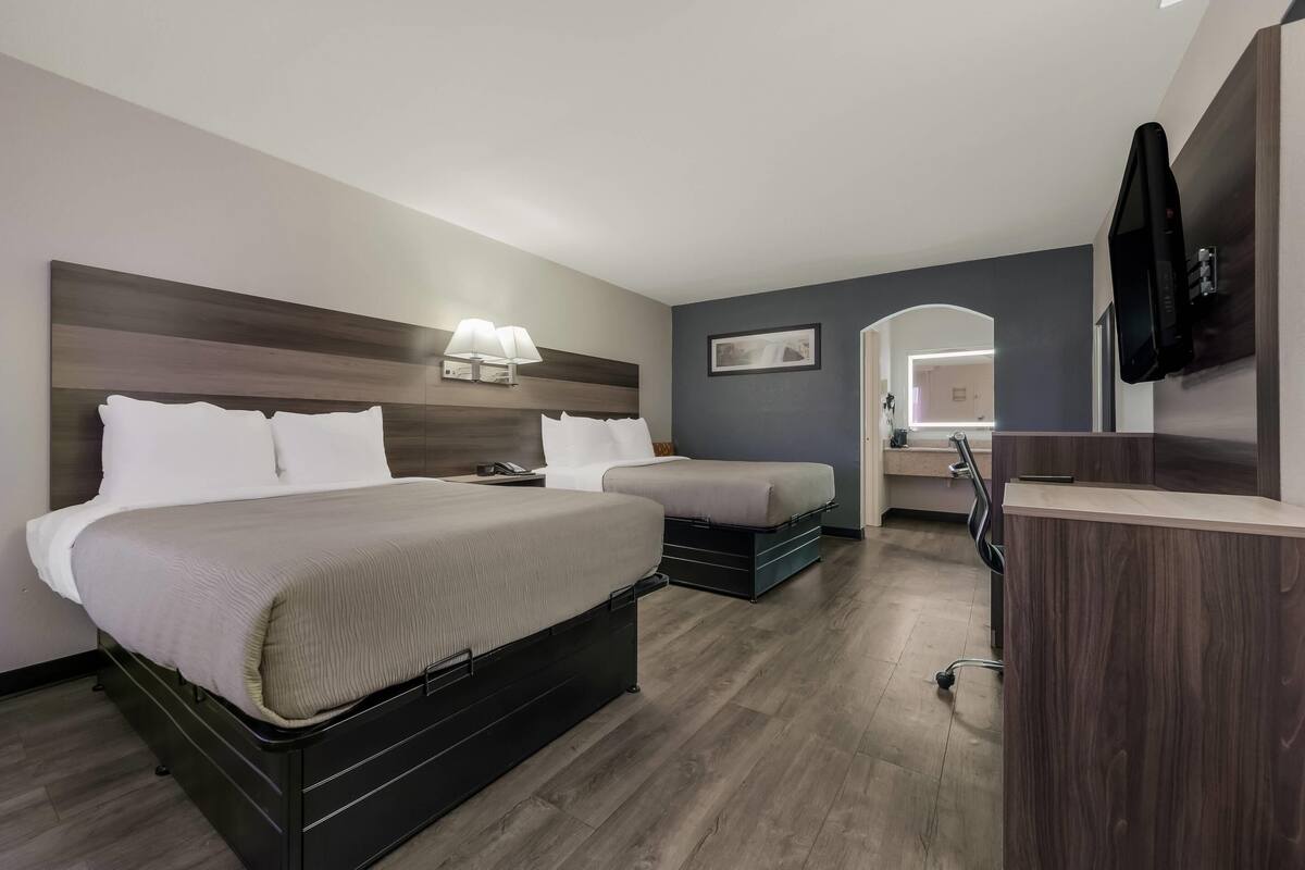 A hotel room with a large bed, a smaller bed, a desk, and a TV.