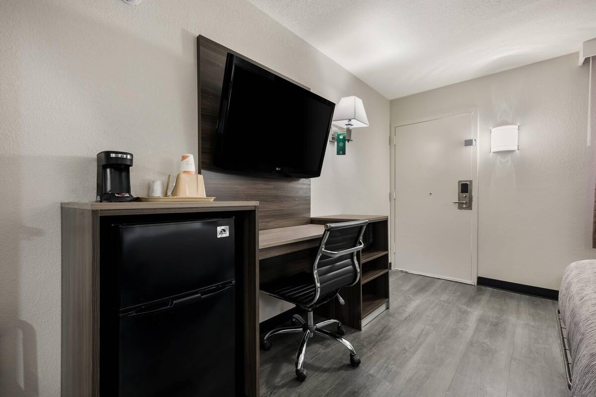 A hotel room with a kitchenette, a flat-screen TV, a desk with a chair, and a bed.
