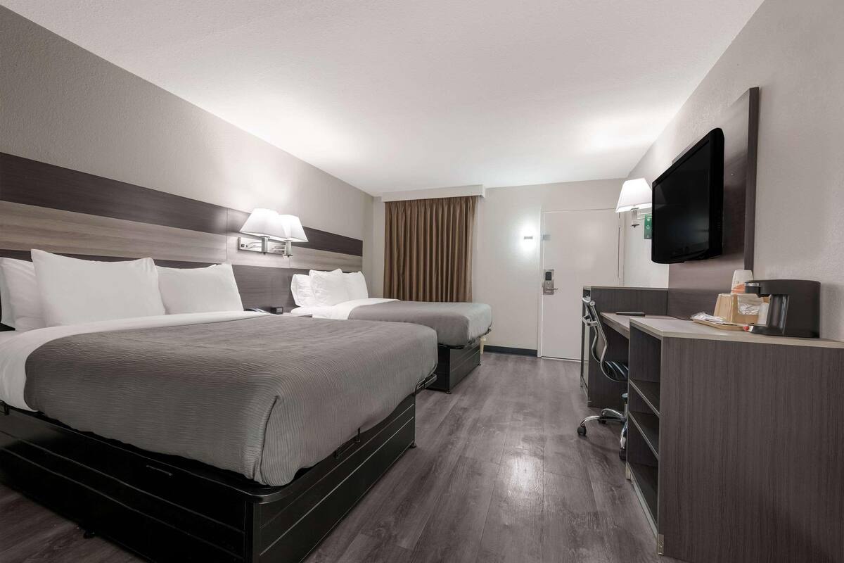 A hotel room with two beds, a desk, a TV, and a window with curtains.
