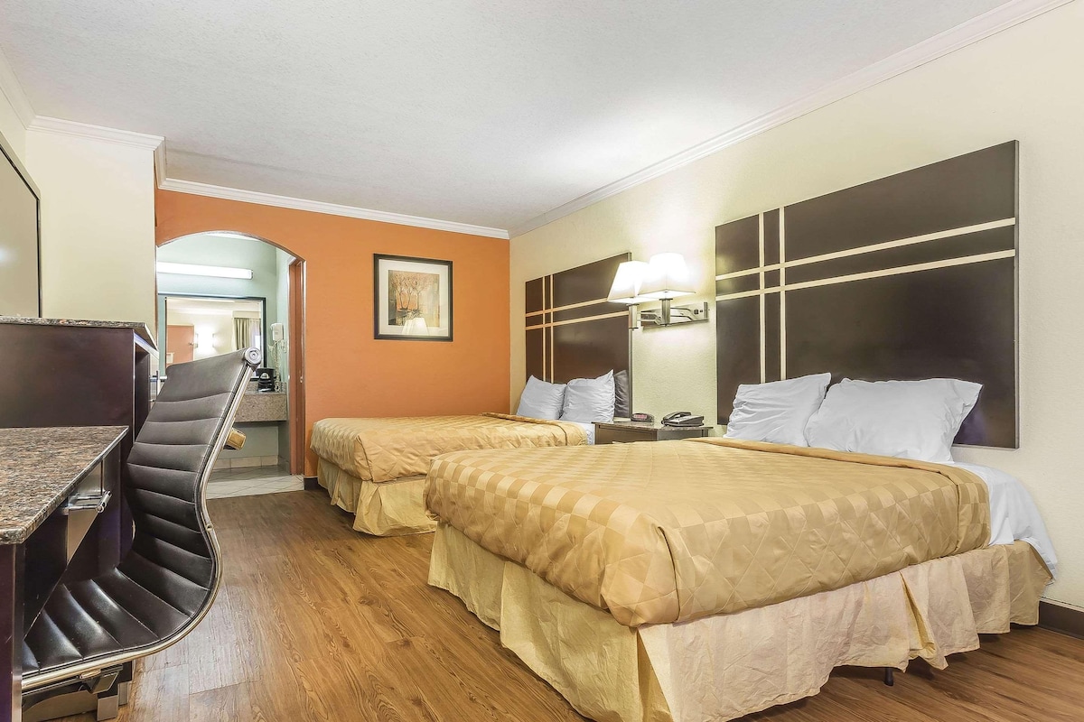 A hotel room with two beds, a desk, and a chair.
