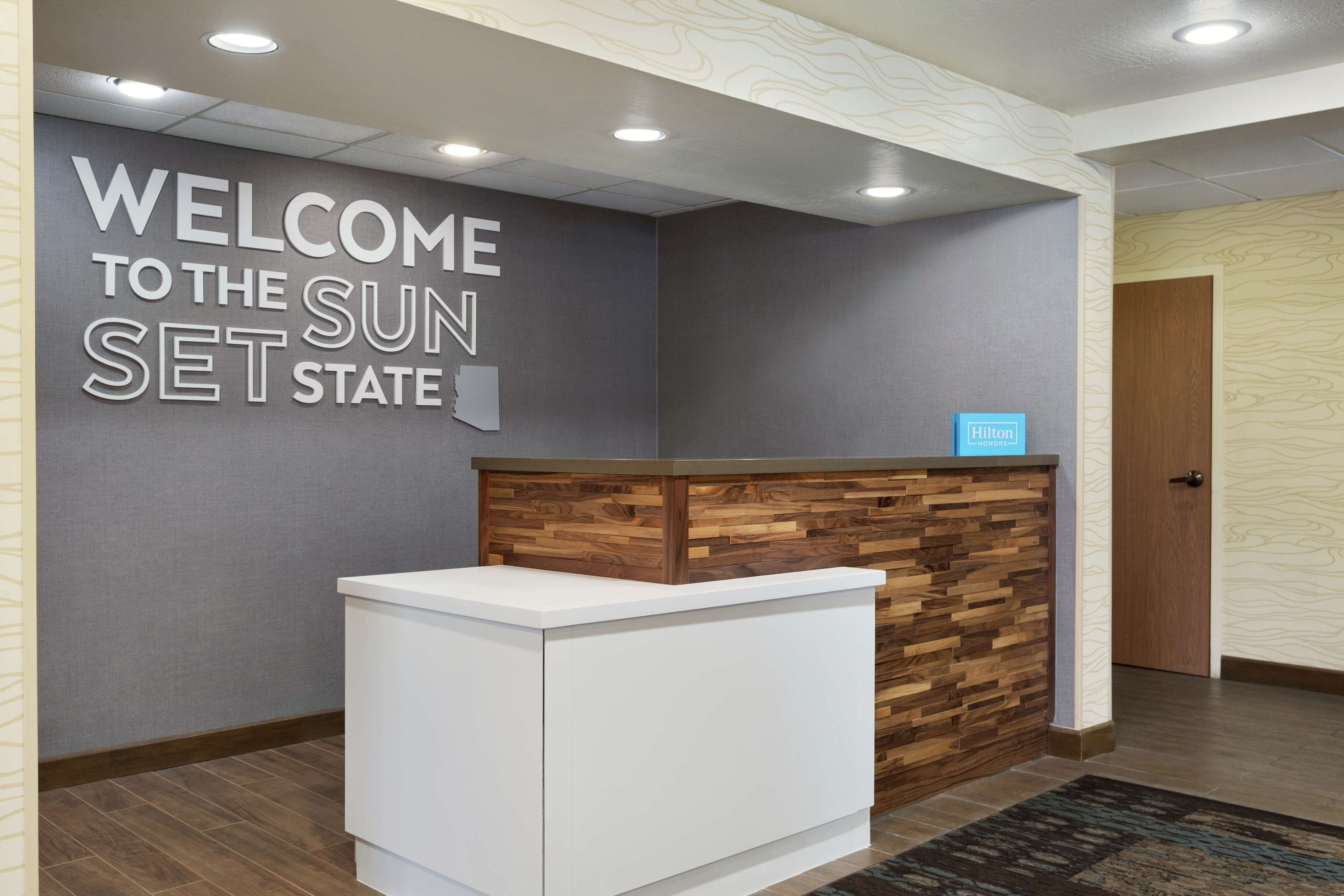 A reception desk with a "Welcome to the Sun Set State" sign, a wooden accent wall, and a "Hilton" sign above the desk.