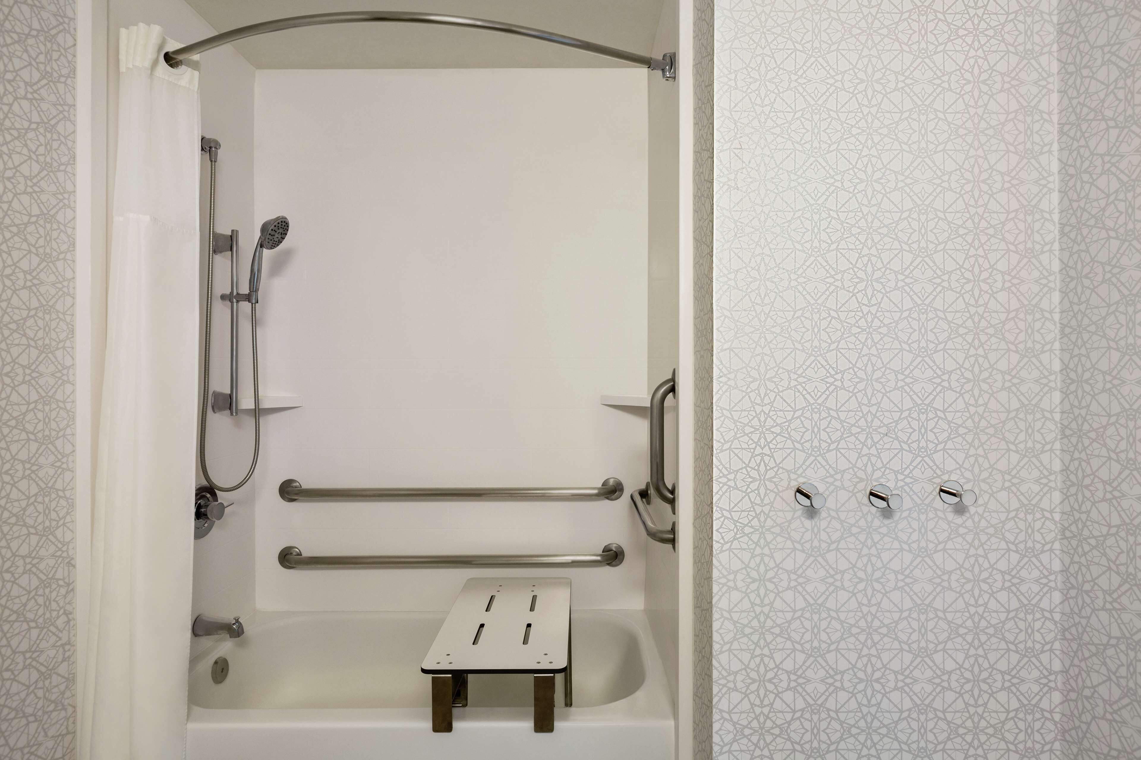 A bathroom with a shower, grab bars, and a small step for accessibility.