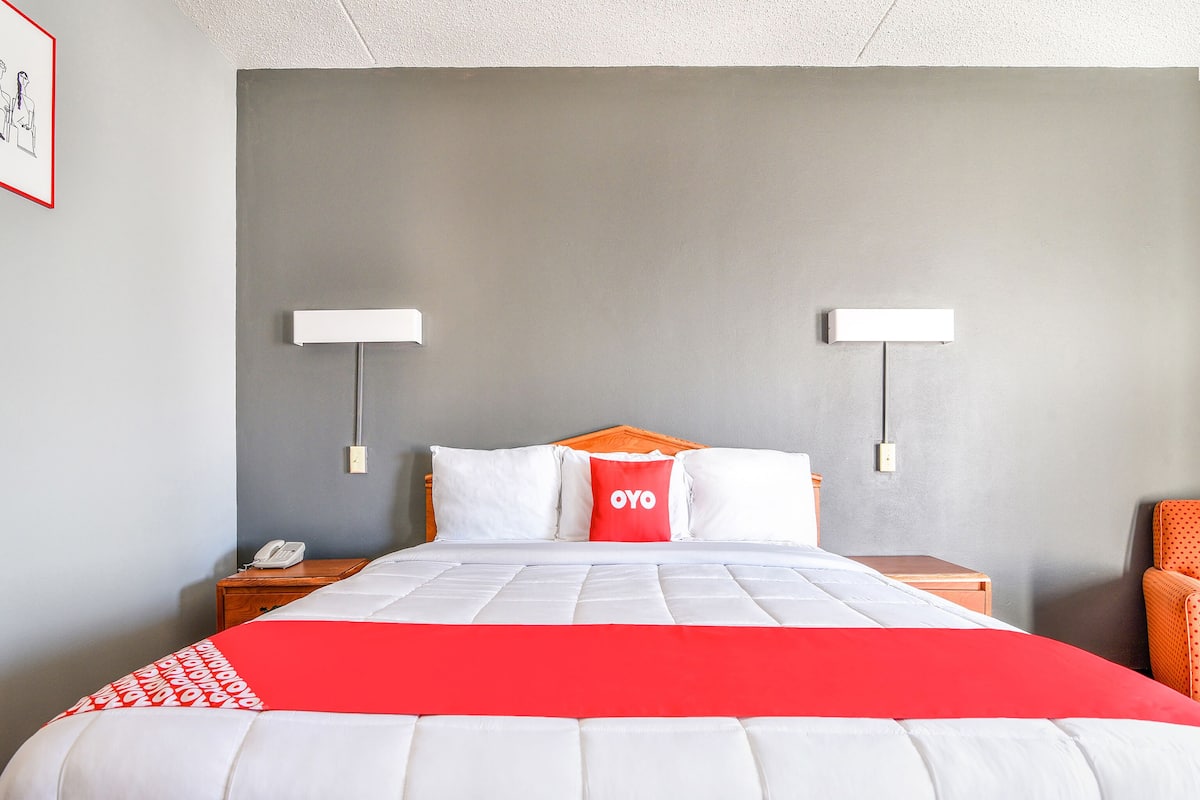 A hotel room with a large bed, two bedside tables, a red and white blanket, and a red pillow with "OYO" text.
