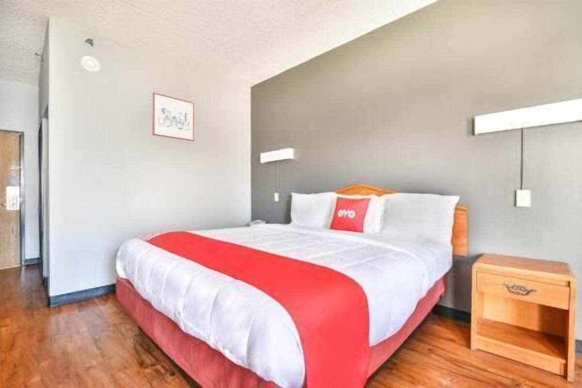 A hotel room with a bed, a nightstand, a wall-mounted lamp, and a framed picture on the wall.