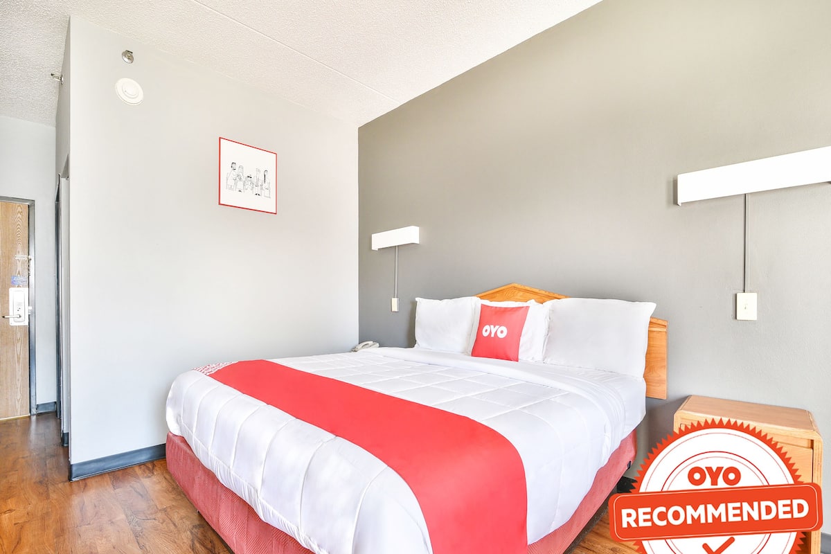 A hotel room with a bed, a nightstand, a wall-mounted lamp, and a framed picture.