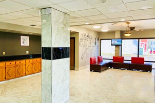 Un vestíbulo con una columna de mármol, armarios de madera, una zona de estar con cojines rojos y una pared con un mural.