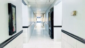 A long, narrow hallway with white tiled floors and walls, black trim, and doors on both sides.