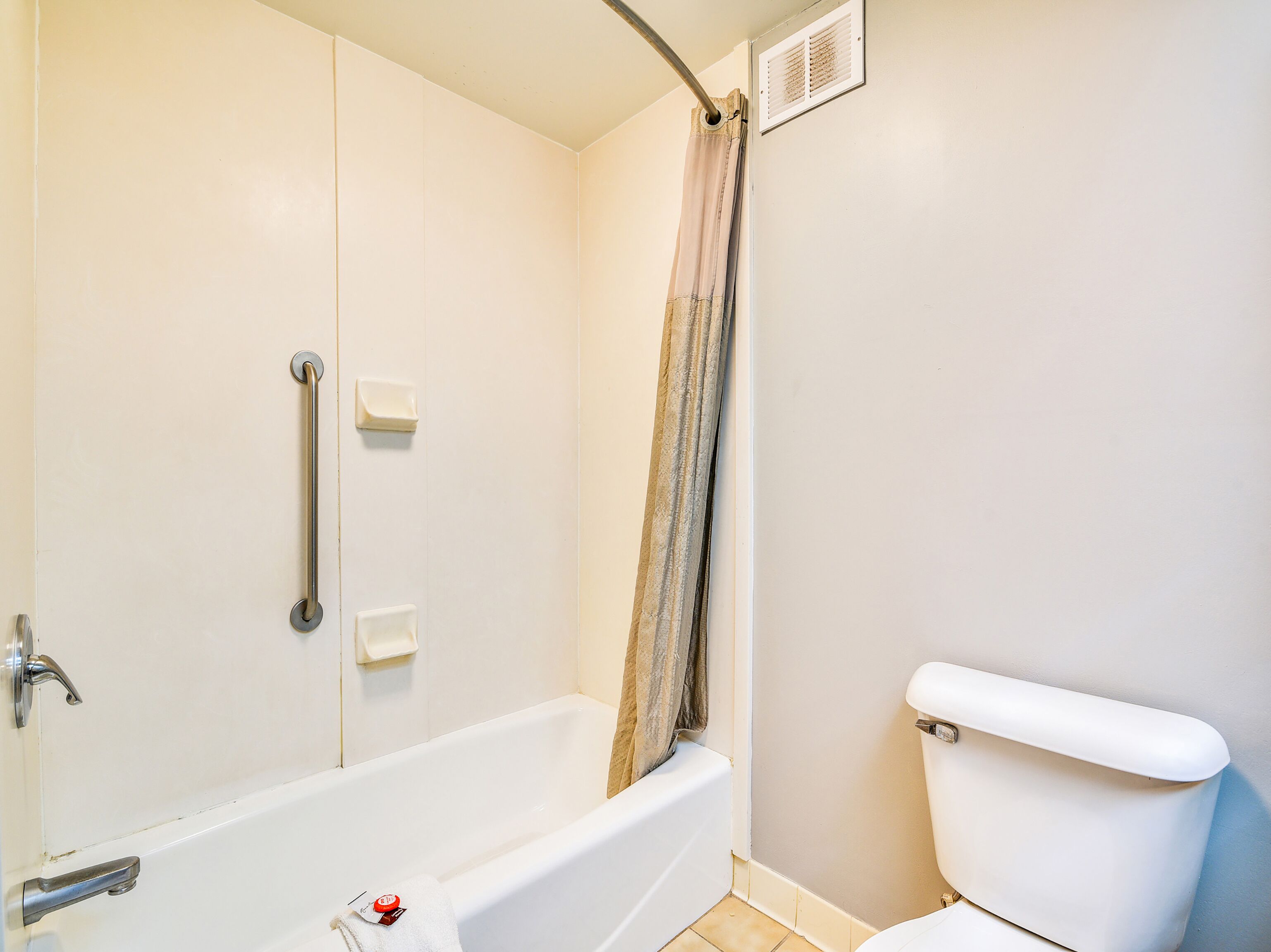 A bathroom with a bathtub, toilet, and handrails.