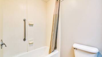 A bathroom with a bathtub, toilet, and handrails.