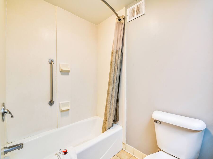A bathroom with a bathtub, toilet, and handrails.