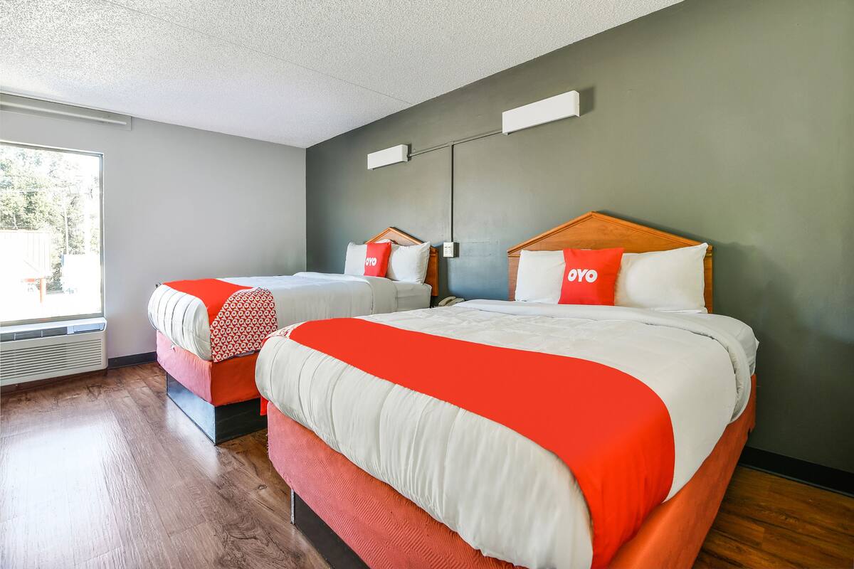 A hotel room with two beds, each with a red and white bedspread, a wooden headboard, and a bedside table with a lamp.