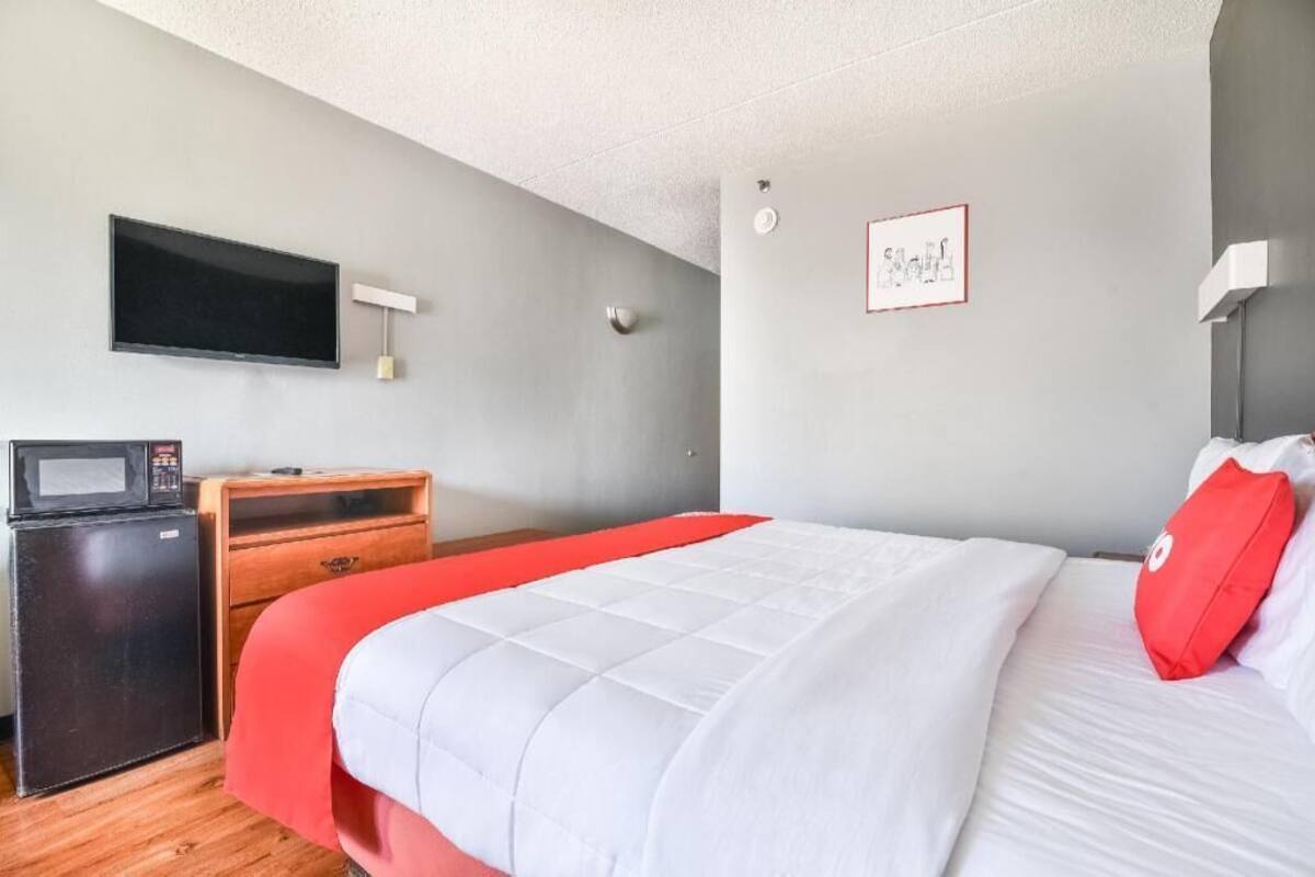 Ein Hotelzimmer mit einem Bett, einem Fernseher, einer Mikrowelle, einem Holzschrank und einem roten Kopfkissen.