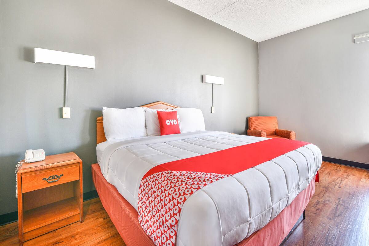 A bedroom with a bed, a nightstand, a chair, and a wall-mounted light fixture.