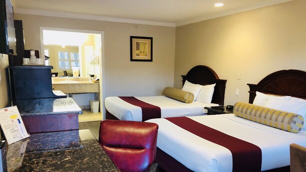 A hotel room with two beds, a desk, a chair, and a bathroom visible through an open door. - Dynasty Suites Hotel Riverside (Riverside)