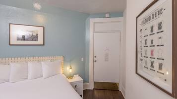 Una habitació d'hotel amb un llit, una taula de nit, un quadre amb una vista urbana i una porta.