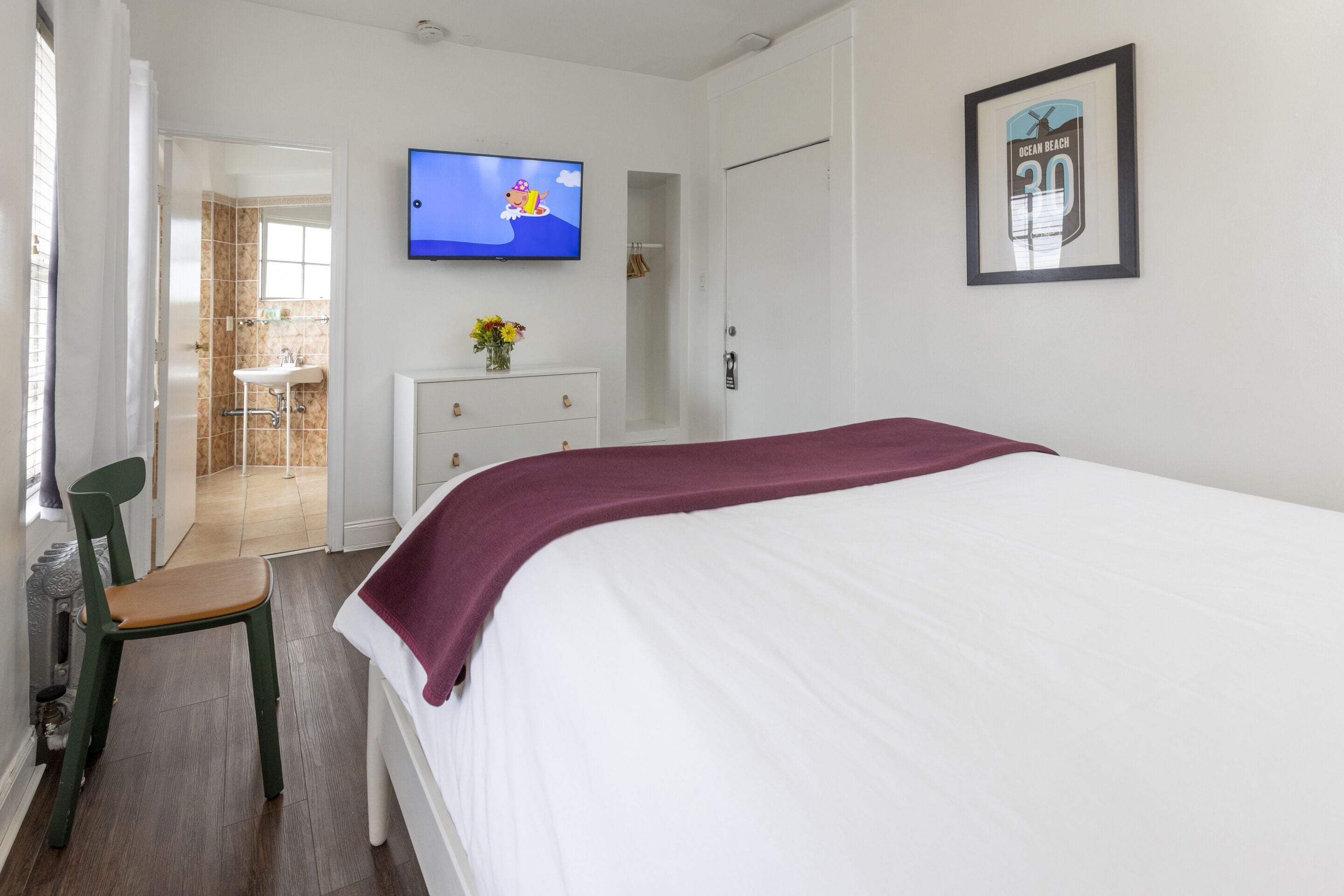 A bedroom with a bed, a TV mounted on the wall, a dresser, and a chair.