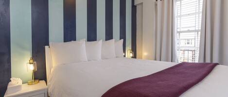 A hotel room with a large bed, a bedside lamp, a nightstand, and a window with curtains.
