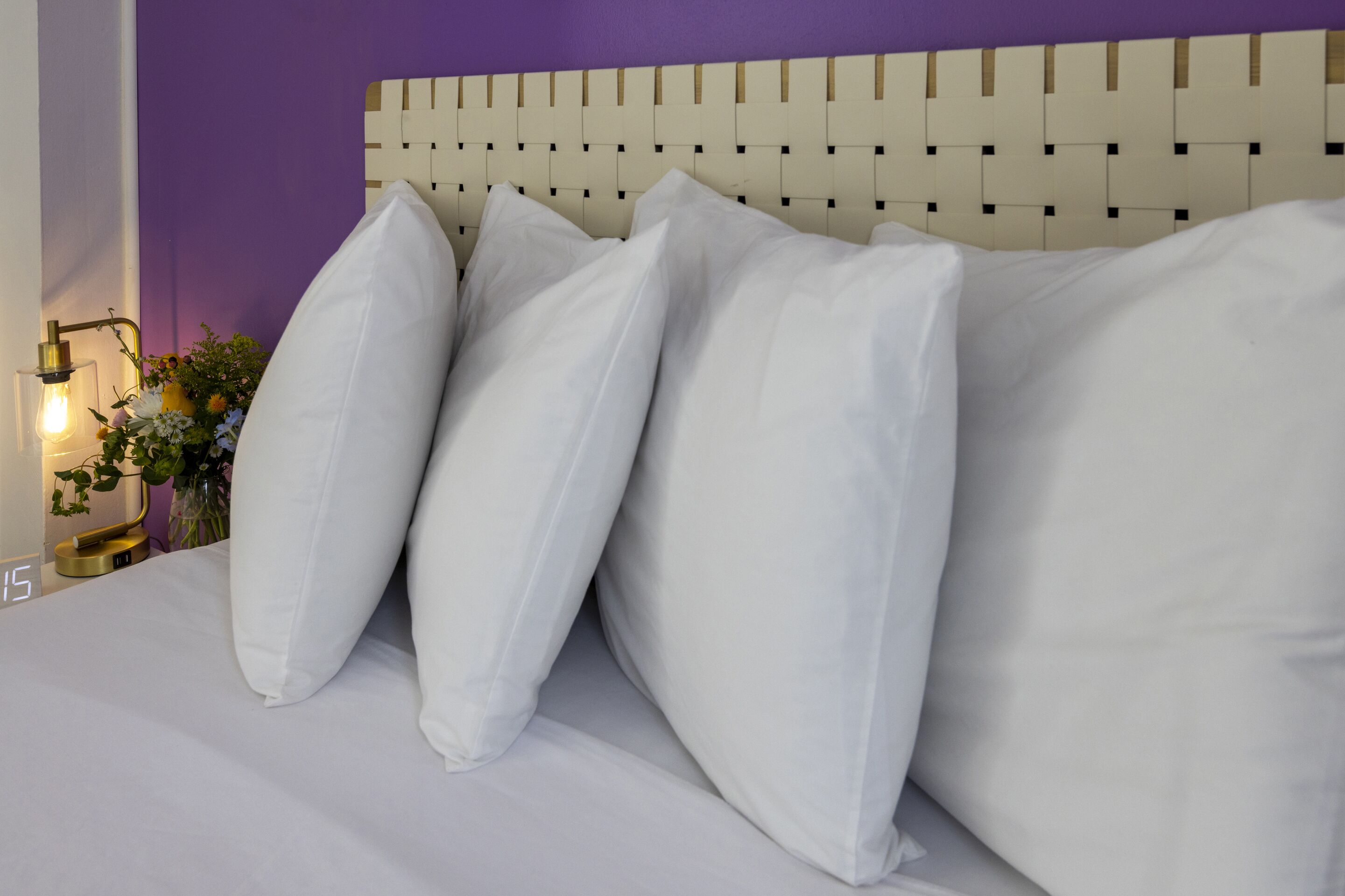Cama com almofadas brancas e cabeceira com padrão trançado.