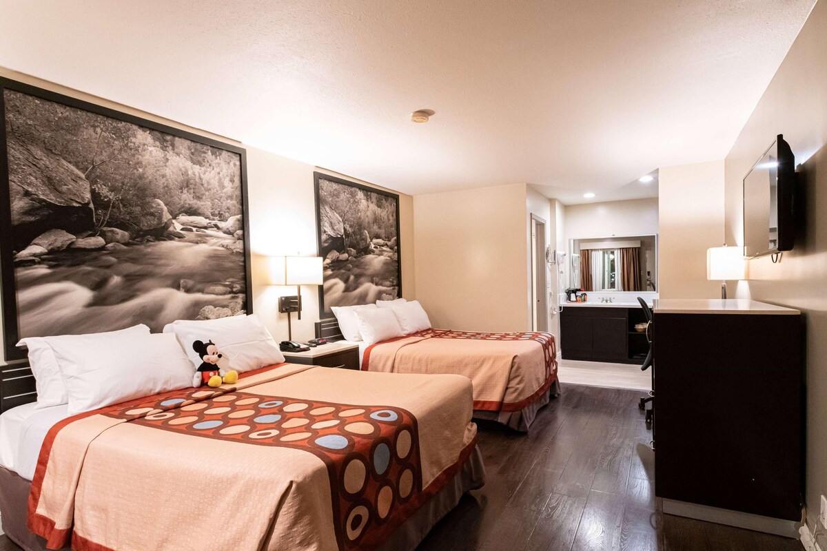 A hotel room with two beds, a desk, a dresser, and a TV.