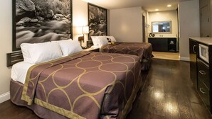 Habitación de hotel con dos camas, un cuadro grande de un río, un escritorio con lámpara y una kitchenette.
