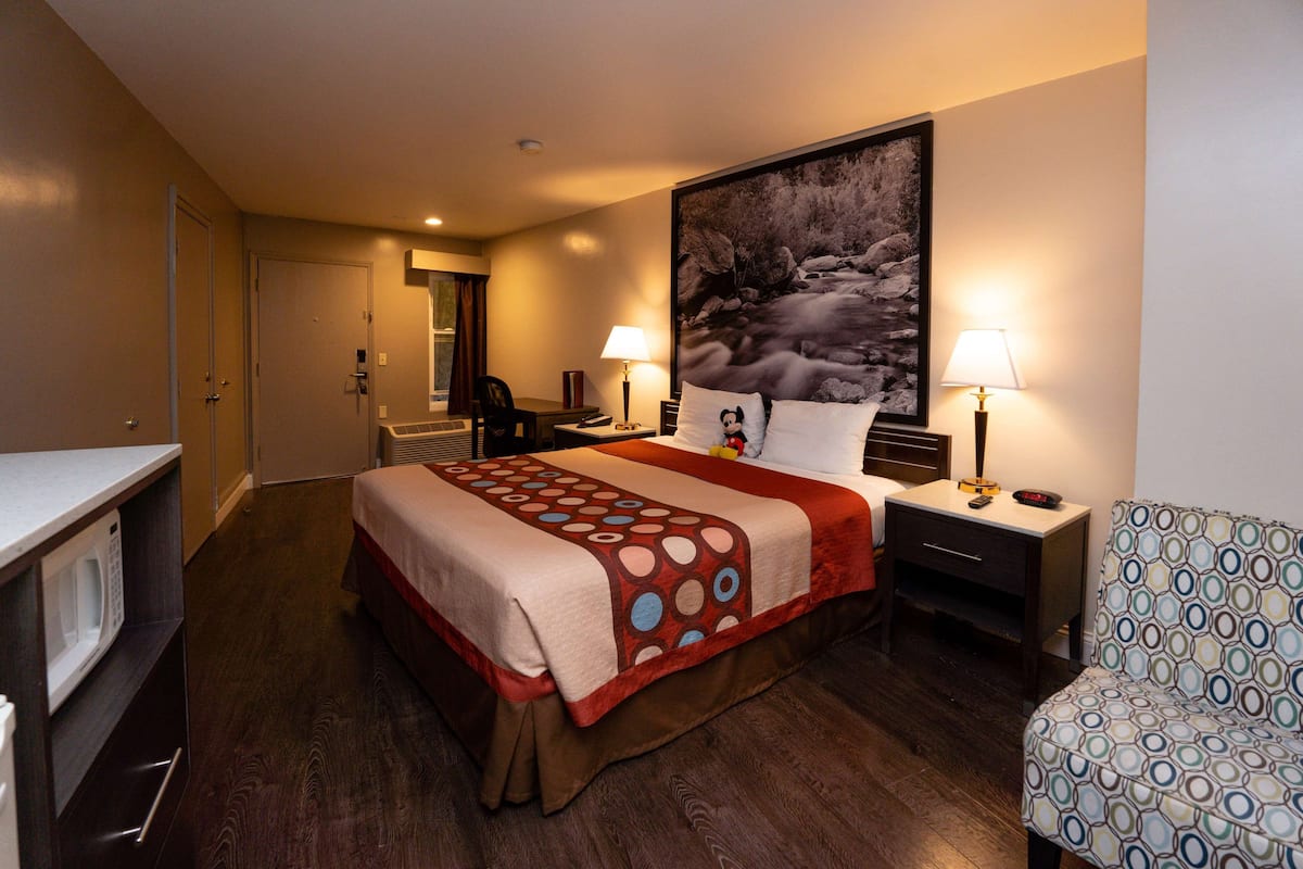 A hotel room with a bed, a desk, a chair, a microwave, and a large painting on the wall.