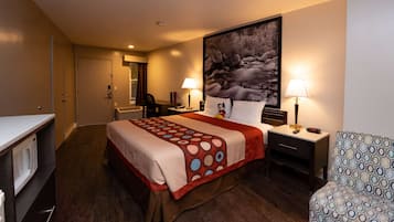 A hotel room with a bed, a desk, a chair, a microwave, and a large painting on the wall.
