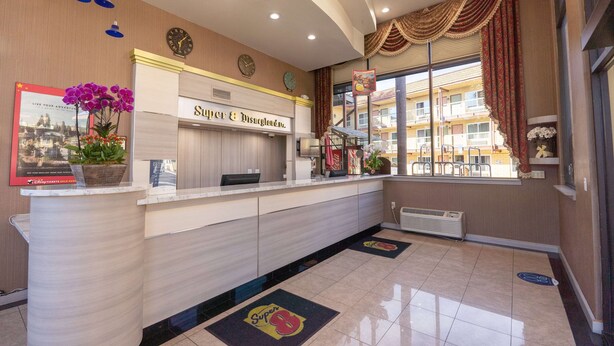Zona de recepción de un hotel, con mostrador, un reloj y un ventanal con cortinas.