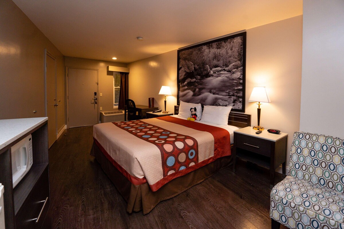 A hotel room with a bed, a desk, a chair, a microwave, and a large painting on the wall.