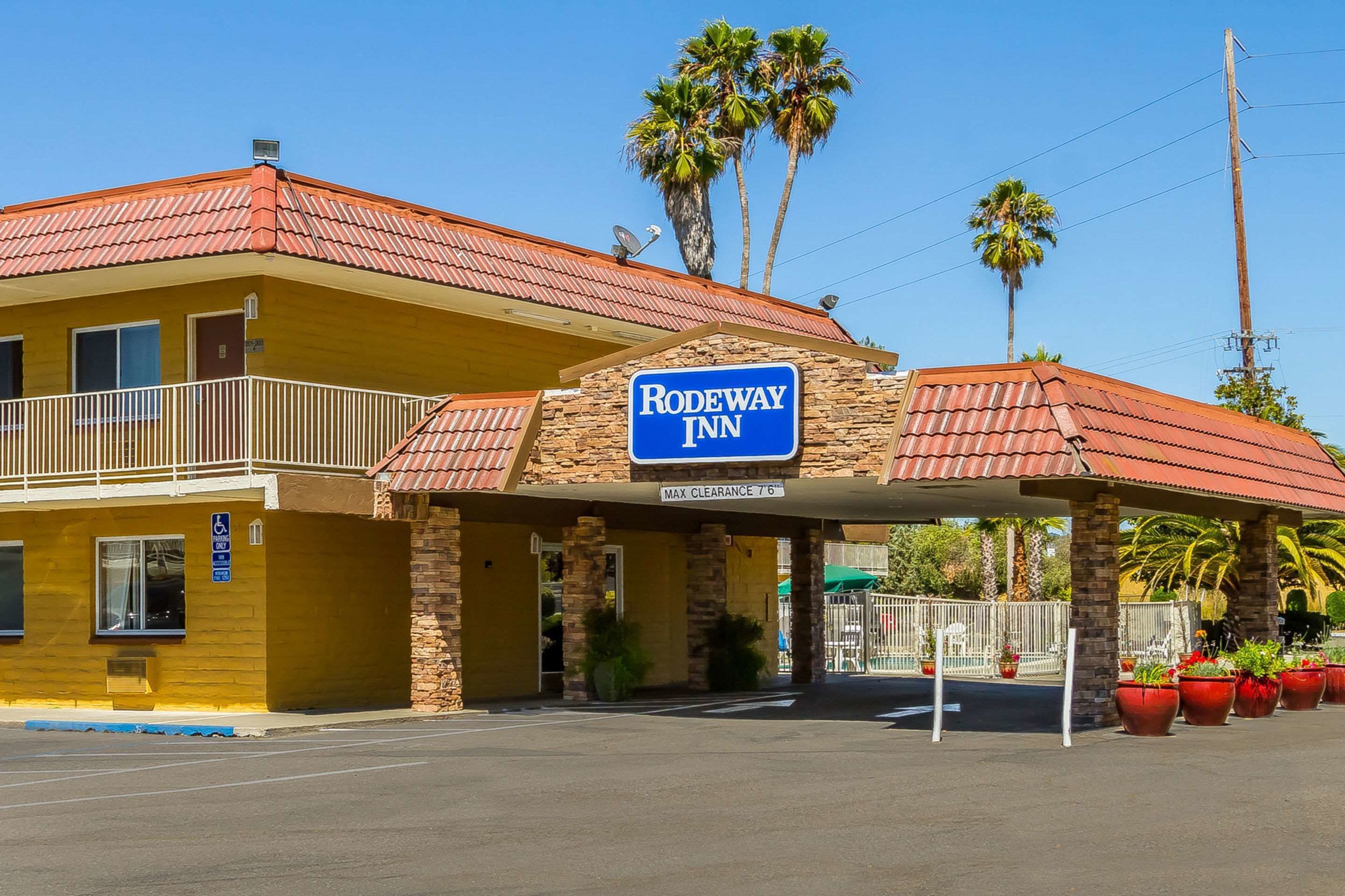 Um Rodeway Inn com telhado de telhas vermelhas, uma placa de identificação e um estacionamento com plantas em vasos.