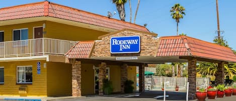 Um Rodeway Inn com telhado de telhas vermelhas, uma placa de identificação e um estacionamento com plantas em vasos.