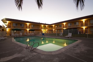A hotel with a swimming pool, outdoor seating, and a fenced area.