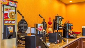 A kitchen area with waffle makers, a syrup dispenser, and a coffee machine. - Rodeway Inn Wine Country (Rohnert Park)