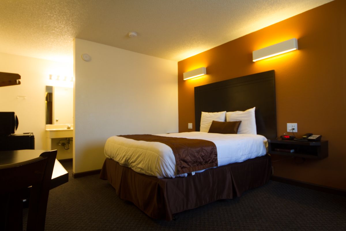 A hotel room with a bed, bedside table, and a desk with a chair.