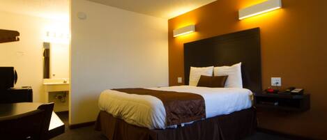 A hotel room with a bed, bedside table, and a desk with a chair.