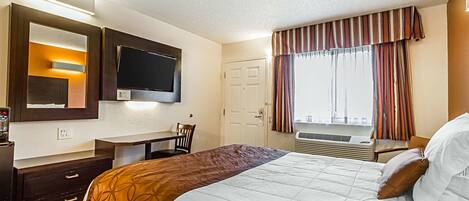 Habitación de hotel con cama, escritorio, televisión, ventana con cortinas y puerta.
