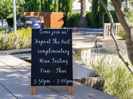 Un letrero anuncia un evento de degustación de vino de cortesía en Napa at The Nest, programado de martes a jueves de 5:30 pm a 7:00 pm.