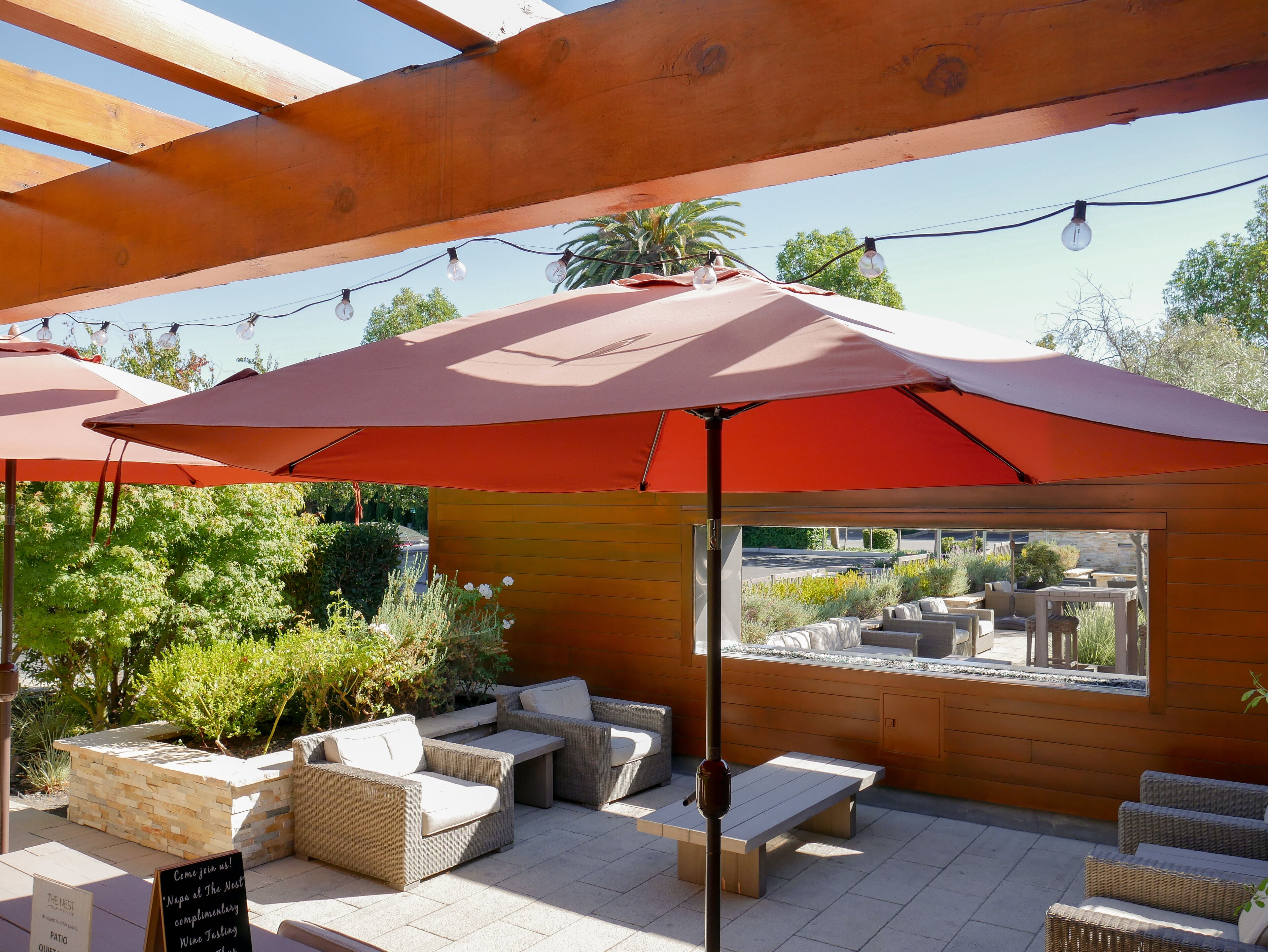 An outdoor patio area with wicker furniture, a stone planter, and a view of a garden.
