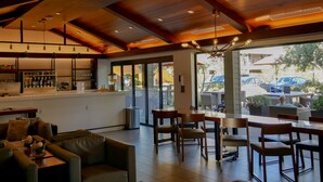 A modern interior with a bar area, seating, and large windows offering a view of the outdoors. - The Nest Hotel Palo Alto (Palo Alto)