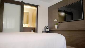 Ein Hotelzimmer mit einem großen Bett, einer Schiebetür, einem wandmontierten Fernseher, einem kleinen Tisch mit Kaffeemaschine und einer Topf-Orchidee.