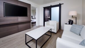 A modern living room with a flat-screen TV, a white sofa, a coffee table, and a sliding door closet. - The Nest Hotel Palo Alto (Palo Alto)