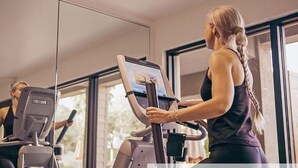 A gym with exercise equipment, including a treadmill and an elliptical machine, and large windows providing natural light. - The Nest Hotel Palo Alto (Palo Alto)
