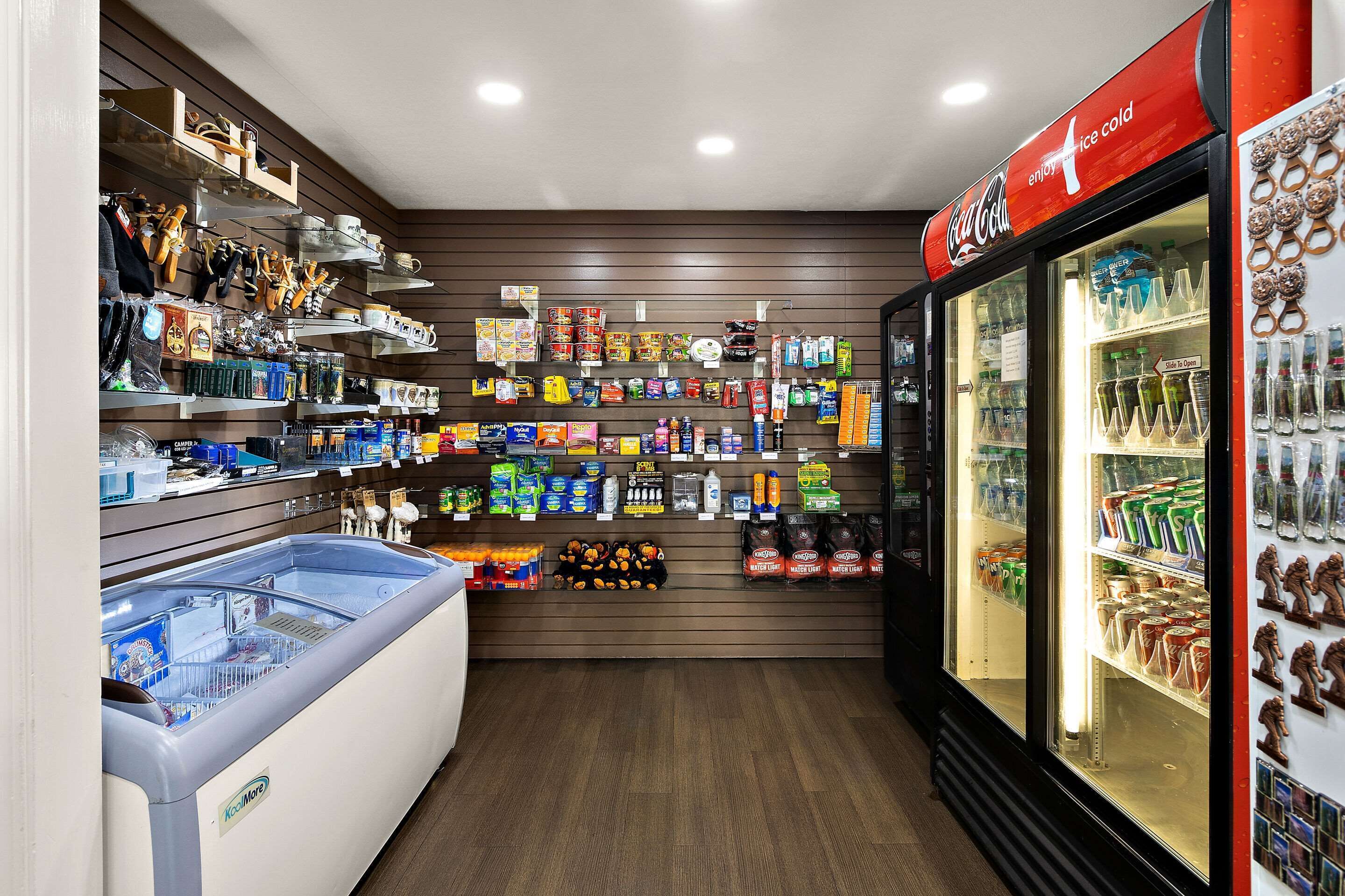 Una tienda con estanterías llenas de diversos productos, un mostrador refrigerado y un refrigerador Coca-Cola.