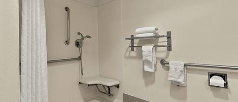 A bathroom with a shower, grab bar, toilet, and towel rack.