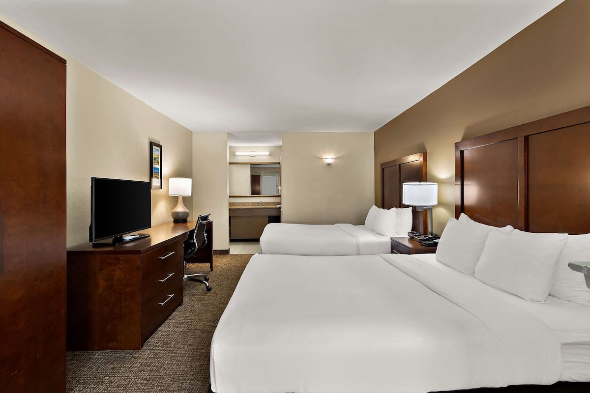 A hotel room with two beds, a desk with a TV, a lamp, and a mirror.