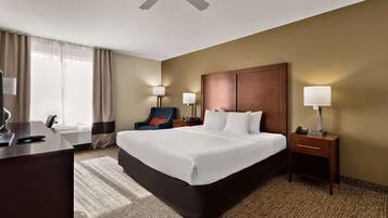 A hotel room with a large bed, a desk, a chair, two bedside lamps, a ceiling fan, and a window with curtains.