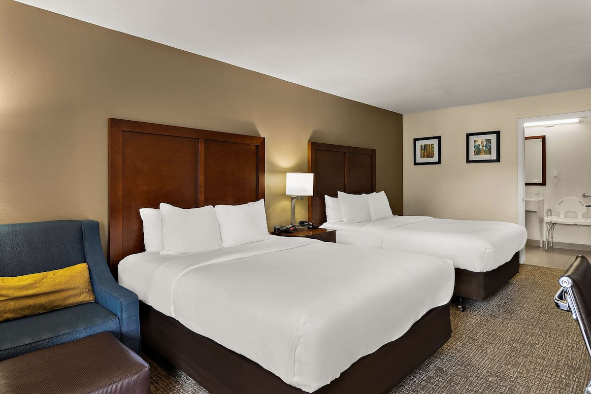 A hotel room with two beds, a sofa, a desk, and a chair.
