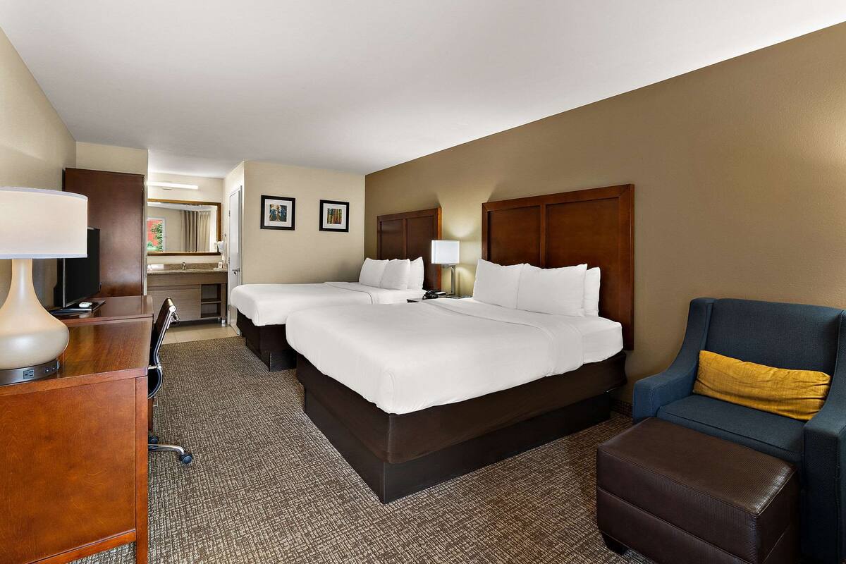 A hotel room with a large bed, a desk, a chair, and a small ottoman.