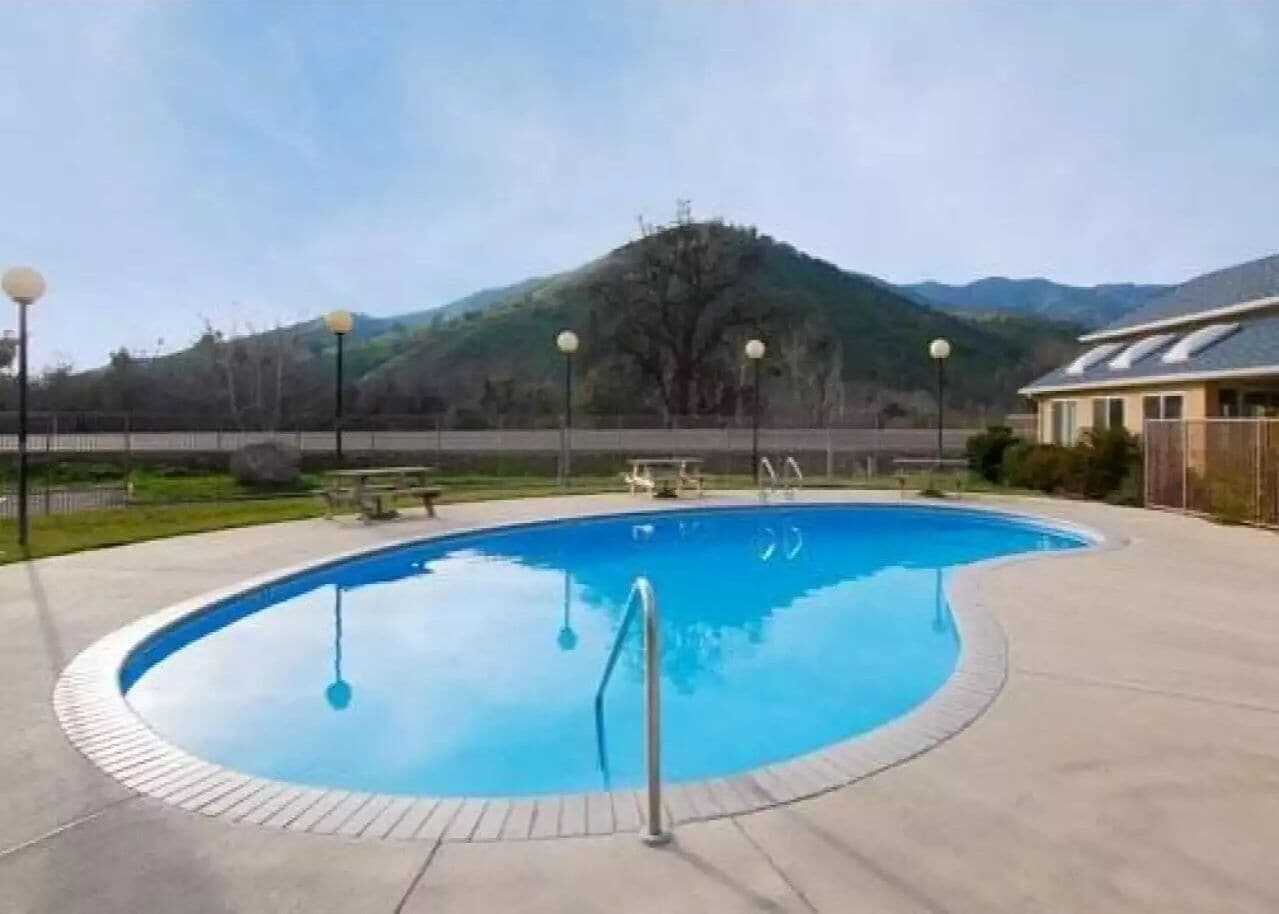 Una piscina con un deck perimetral, una escalera metálica y montañas al fondo.